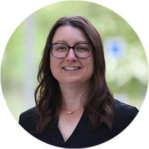 Dr Jillian Rickly, a woman with long brown hair and glasses wearing a smart black top and smiling at the camera