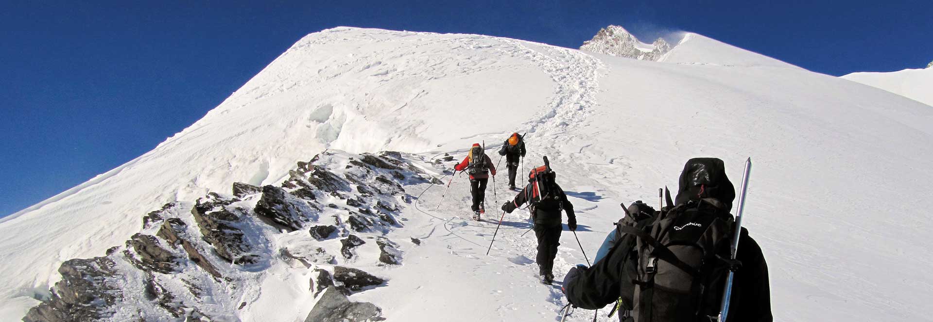 Grupo de senderistas avanzando por una ladera nevada de alta montaña
